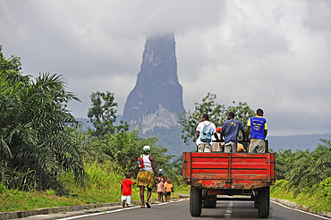 Woman and child walking on southern road as a truck is passing, with the Pico Cao Grande (Great Dog Peak) in the background,southern part of Sao Tome Island, Republic of Sao Tome and Principe,Africa