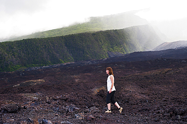 Woman walking on cold lava flow on the coast named 'Le Grand Brule' on the Southeast part of Reunion island, Overseas departement of France, Indian Ocean