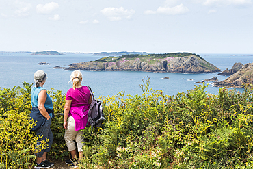 Two women looking at the Brecquou island from La Coupée, the narrow isthmus which links Greater and Little Sark, Sark island, Channel Islands, Bailiwick of Guernsey, United Kingdom