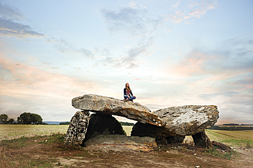 Young girl sitting on a Megalithic Dolmen at sunrise, locality Le Carroir Bon Air, commune of Ligre, near Chinon and Richelieu,Indre-et-Loire department, Centre region,France, Europe