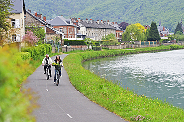 Young woman and a man cycling on cycle lane along the Meuse River at Haybes,Ardennes department,Champagne-Ardenne region of northeasthern France,Europe