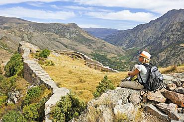 Young woman sitting on a defensive wall of Smbataberd Fortress, on the crest of a hill between the villages of Artabuynk and Yeghegis, near Yeghegnadzor, Vayots Dzor province, Armenia, Eurasia