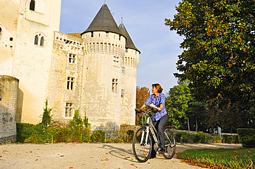 Young woman cycling in front of the Castle St-Jean, Nogent-le-Rotrou, Parc naturel regional du Perche, Eure-et-Loir, Cengre-Val-de-Loire, France, Europe