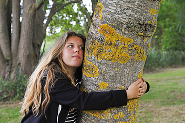 Young girl embracing the trunk of an ash tree, France, Europe