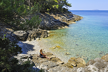 Woman sitting on rocks at a creek of Mrcara islet at the north-west of Lastovo island, Croatia, Southeast Europe