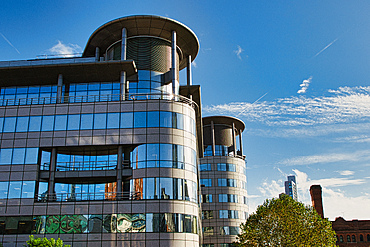 Two modern office buildings with a rounded, curved design and many large windows, set against a clear blue sky with white clouds. The building on the left is in focus in Manchester, UK.