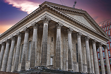 A low-angle view of a classical-style building, featuring numerous large grey columns and intricate stonework, set against a twilight sky. A modern building is partially visible in the background in Birmingham, UK.