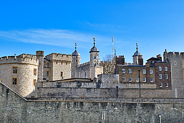 Exterior view of the Tower of London, showcasing various stone structures, including towers, walls, and buildings, under a clear blue sky