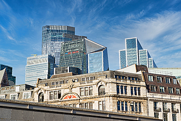 Modern skyscrapers and older, ornate buildings stand side-by-side against a bright blue sky with scattered clouds. The contrast between architectural styles is striking in London, UK.