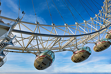 Close-up view of the London Eye Ferris wheel's structure and passenger capsules against a clear blue sky. The image showcases the wheel's framework, cables, and several visible capsules.