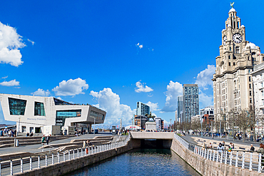 View of Liverpool waterfront featuring the Royal Liver Building, a modern museum, and a canal under a blue sky with scattered clouds.
