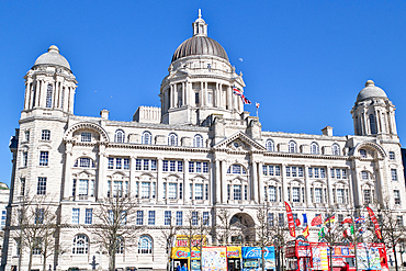 The image shows the Royal Liver Building in Liverpool, a large, ornate building with a clear blue sky as the background. Tour buses are in the foreground.