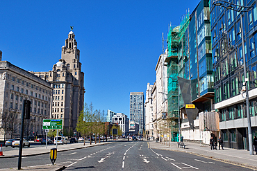 City street view featuring historic and modern architecture under a clear blue sky on a sunny day with light traffic in Liverpool, UK.