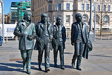 Bronze statues of The Beatles walking in a line. Building and scaffolding in the background. Outdoor scene, city setting, daylight in Liverpool, UK.