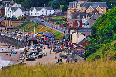 Elevated view of a crowded beach and seaside town with buildings, trees, and beachgoers in Filey, UK.