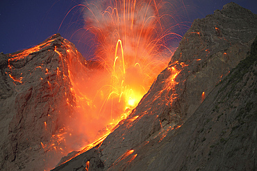 November 28, 2012 - Explosive strombolian type eruption of Batu Tara volcano, Komba Island, Indonesia. Trajectories of red glowing lava bombs are visible against blue night sky.