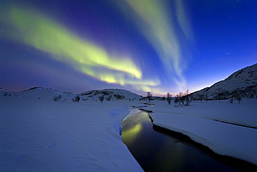 Aurora Borealis over Skittendalen Valley and the Skittendalen River in Troms County, Norway. Auroras are the result of the emissions of photons in the Earth's upper atmosphere.