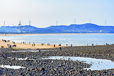 Contrast of rocky and sandy beach coastal recreation area with windmills in the background. Pingtan Island, Fuzhou City, Fujian Province, China.