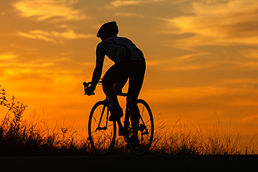 Sports and outdoor activities concept.Silhouette of cyclist riding a road bike on open road in evening during sunset.