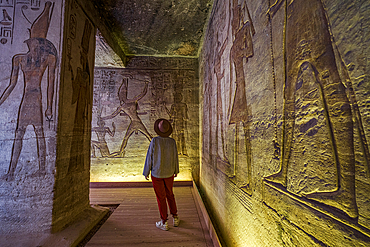 Woman looking at the ancient colorful carved paintings on walls inside the Temple of Nefertari, Abu Simbel, Aswan, Egypt