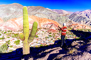 Tourist snapping a selfie with smartphone standing on hilltop above the village of Purmamarca, Argentina