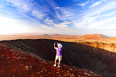 Cheerful man with hat snapping a selfie with smartphone on top of Calderon Hondo volcano, Fuerteventura, Canary Islands, Spain