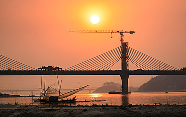 Fishermen fishing next to under construction bridge over Brahmaputra river during sunset, in Guwahati, Assam, India