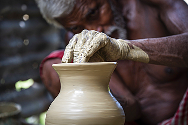 A potter shaping pot from lump of clay on potters wheel at pottery