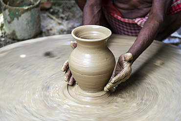 A potter shaping pot from lump of clay on potters wheel at pottery