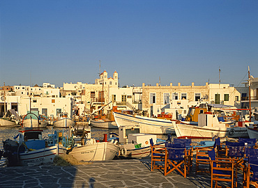 Tables and chairs on quayside, with boats in harbour in the town of Naousa on Paros, Cyclades, Greek Islands, Greece, Europe