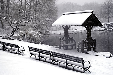 A view of Central Park including benches and a lakeside shelter during a snowstorm, New York City, USA, North America