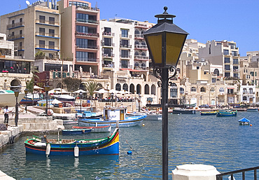 Modern highrise buildings, cafes and old fishing boats in the harbour at St Julian's Bay, Malta, Mediterranean, Europe