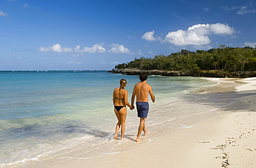 A couple walking along a small sandy beach near the Hotel Melia Rio de Oro, Carretera Guardalavaca, Cuba, West Indies, Central America