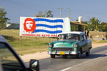 A vintage 1950's American Chevrolet on the road near Trinidad passing a colourful revolutionary road sign, Cuba, West Indies, Central America