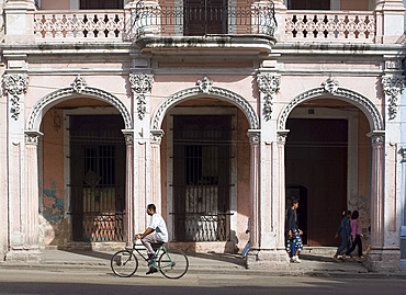 A cyclist passing an ornate old building on Avenida Reina in central Havana, Cuba, West Indies, Central America