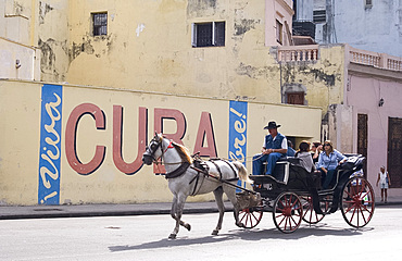 Tourists in a horse carriage passing a wall sign saying 'Live free Cuba', Havana, Cuba, West Indies, Central America