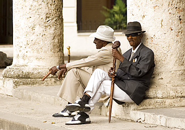 Two Cuban men in vintage forties clothes and smoking cigars while waiting for tourist photographers in Plaza de la Catedral, Habana Viejo, Havana, Cuba, West Indies, Central America