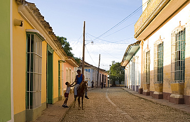 Man on horseback and boy on a cobbled street of pastel coloured houses, Trinidad, Cuba, West Indies, Central America