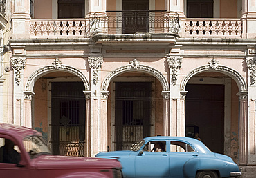 Two vintage cars passing an ornate building on Avenida Reina in central Havana, Cuba, West Indies, Central America