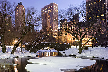 The Gapstow Bridge in Central Park after a snowstorm with skyscrapers behind at dusk, New York City, New York State, USA