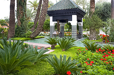 An ornately tiled pavilion surrounded by geraniums and palm trees in the garden of La Mamounia Hotel in Marrakech, Morocco, North Africa, Africa