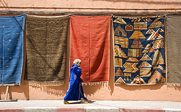 A woman in Islamic dress walking by a wall hung with carpets in the Medina in Marrakech, Morocco, North Africa, Africa