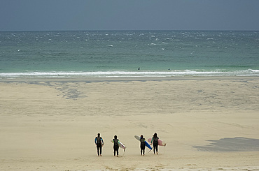 Four surfers in wet suits carrying boards and heading down the beach toward rough seas on a windy day in St. Ives, Cornwall, England, United Kingdom, Europe