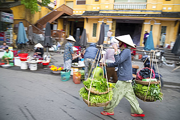 A woman walking through the market with heavy baskets of vegetables in Hoi An, Quang Nam Province, Vietnam, Indochina, Southeast Asia, Asia