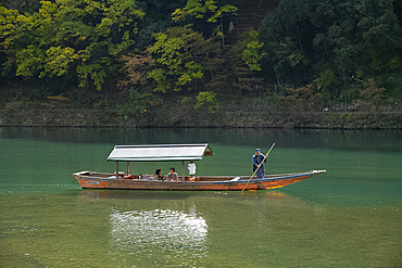 Tourists sightseeing in a small wooden boat on the Oi River in the Arashimaya region outside Kyoto, Japan, Asia