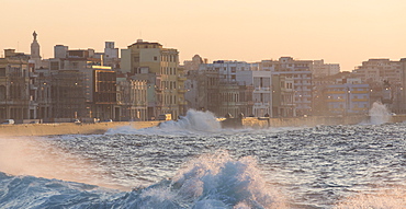 Buildings along The Malecon bathed in soft evening sunlight with large waves crashing against the sea wall, The Malecon, Havana, Cuba, West Indies, Caribbean, Central America