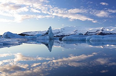 View over Jokulsarlon, a glacial lagoon at the head of the Breidamerkurjokull Glacier, towards icebergs and snow-capped mountains, with reflections in the calm water of the lagoon on a winter's afternoon, on the edge of the Vatnajokull National Park, South Iceland, Iceland, Polar Regions