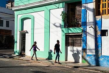 Man and woman (and their shadows) walking through colouful buildings, Old Havana, Cuba