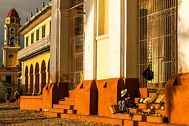 Evening sunlight bathes buildings of main square and souvenir seller on Cathedral steps, Trinidad, Cuba