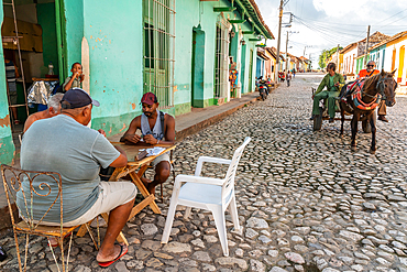 Dominoes game by the corner shop while a horse and cart go by on cobblestones, Trinidad, Cuba